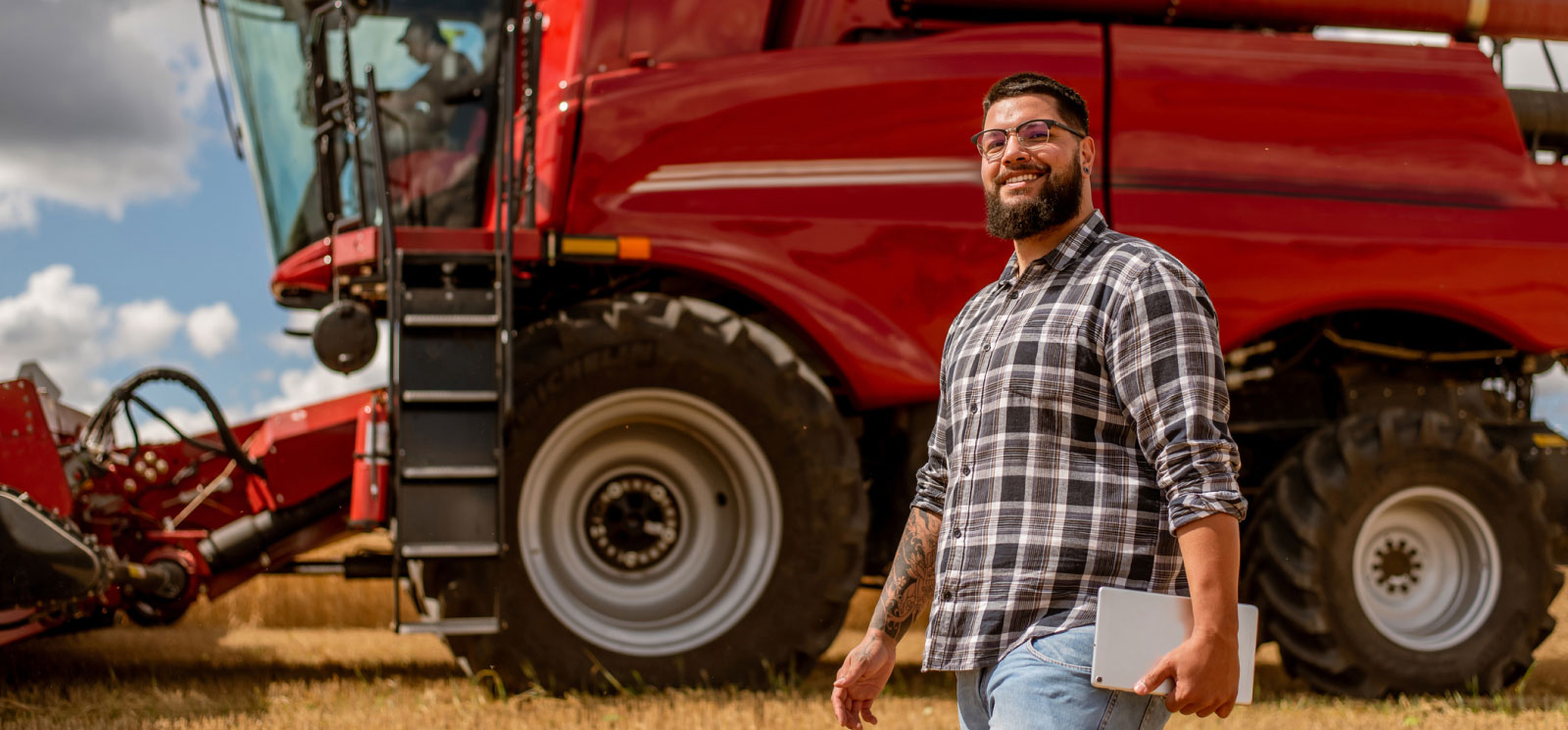 A man holding a tablet and walking in front of large farm equipment